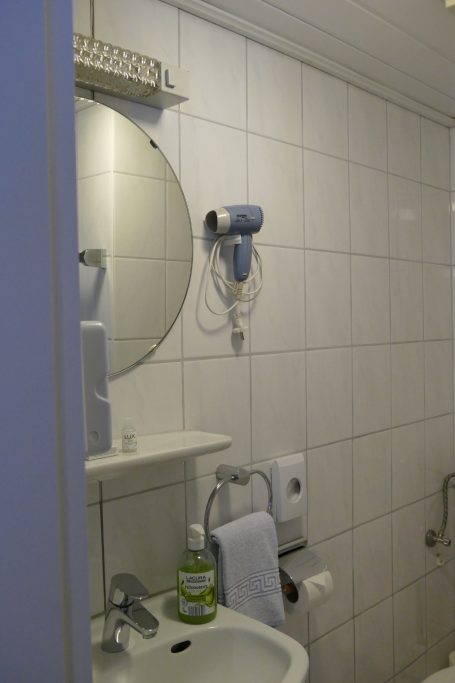Badezimmer mit Waschbecken, Spiegel, Handtuchhalter und Fön an der Wand.